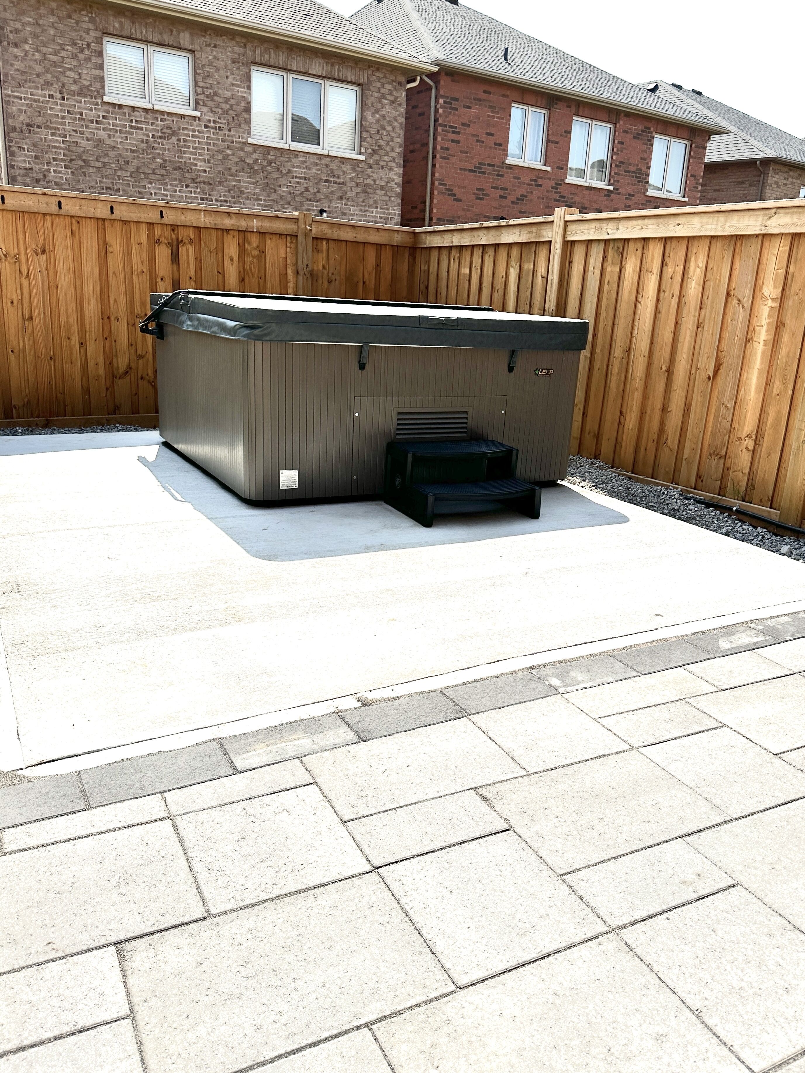 Un jacuzzi en un patio trasero con una valla de madera y una casa de ladrillo al fondo.