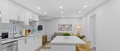 A modern kitchen with white cabinetry, a marble countertop, and a built-in dishwasher.