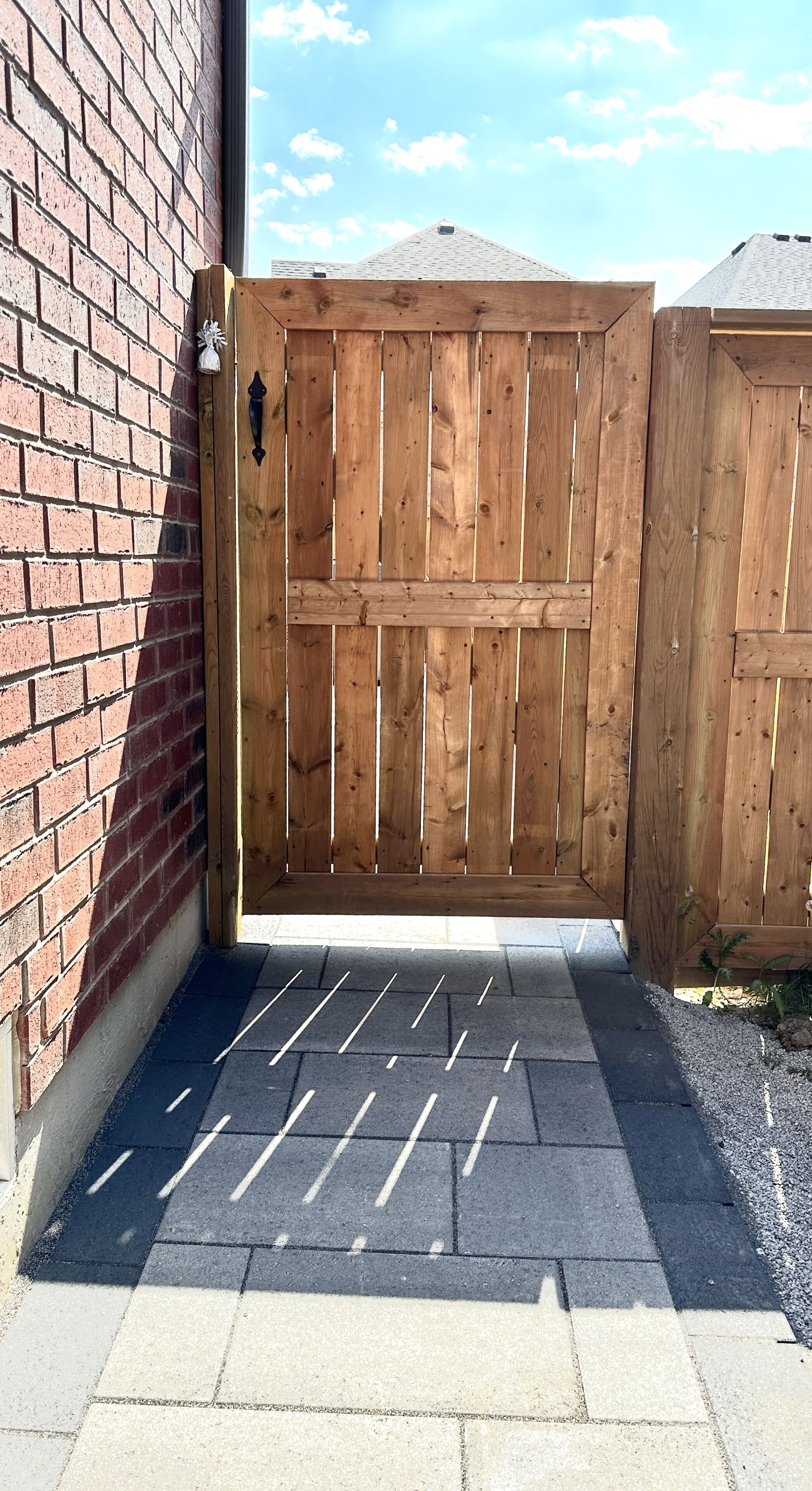 A wooden gate with a metal latch, a brick wall, and a paved entrance.