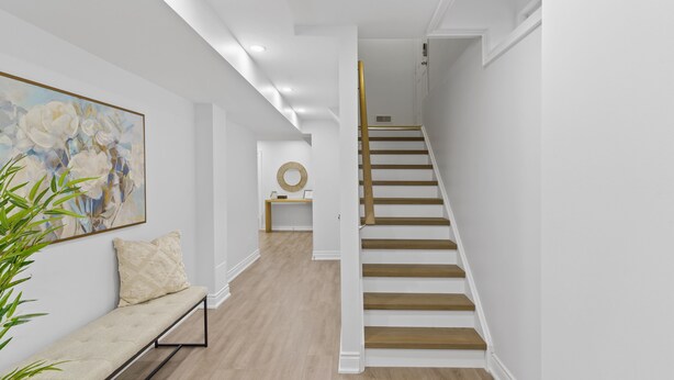 Una escalera de madera con barandillas blancas que conduce a una habitación con piso de madera y un banco con cojín.