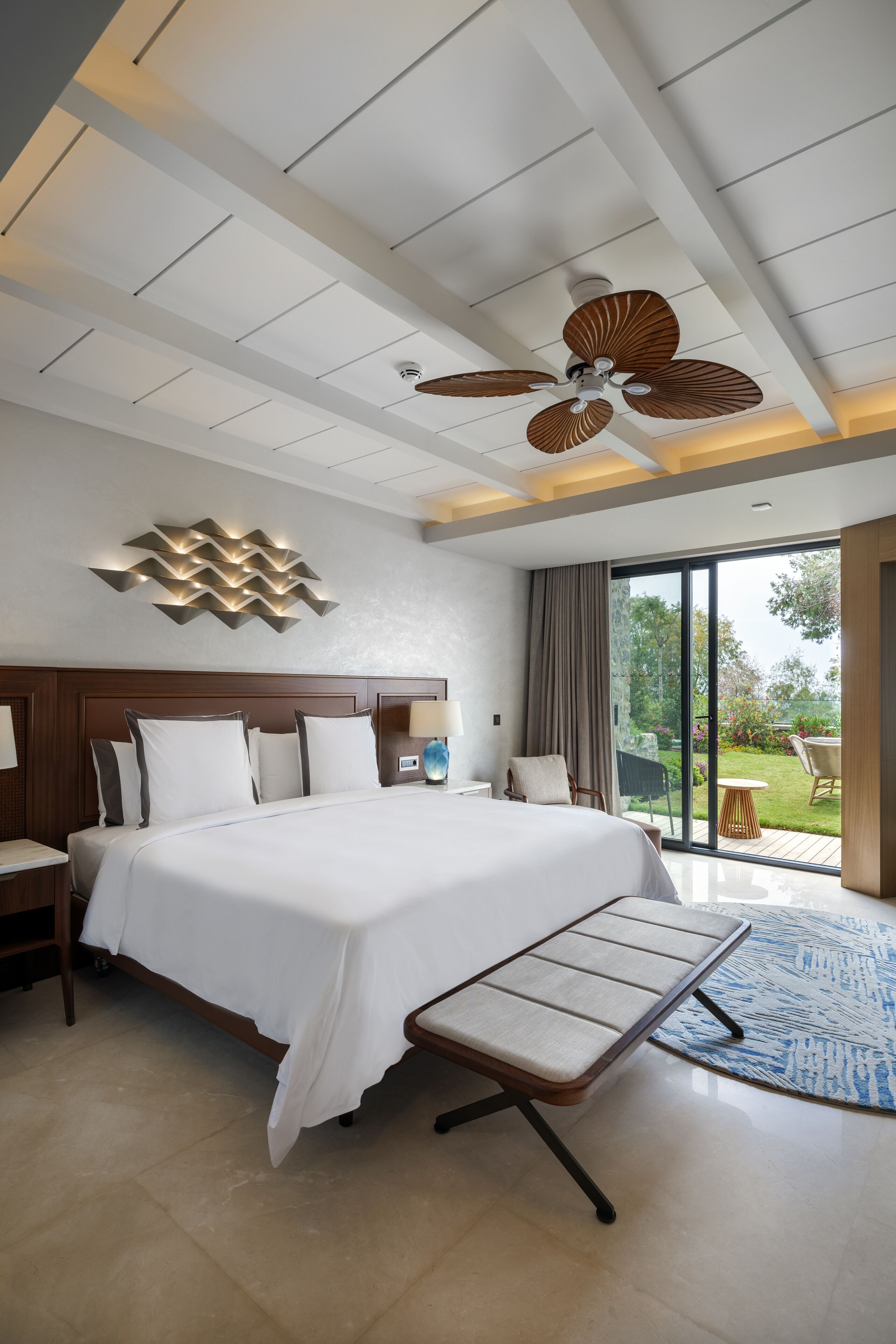 Une chambre d’hôtel moderne dotée d’un grand lit, d’un ventilateur de plafond, d’une vue sur le jardin et d’une grande fenêtre.