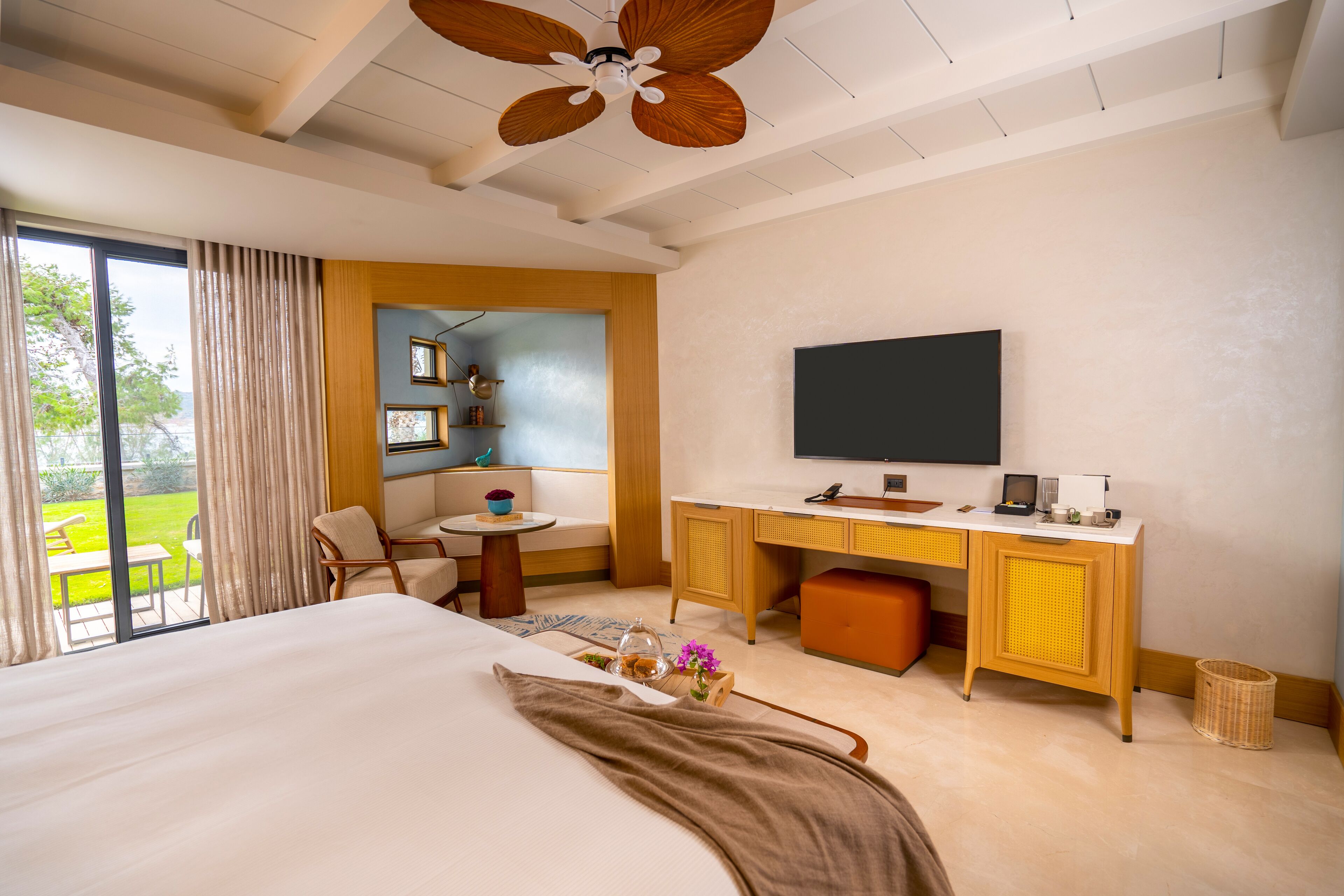 A hotel room with a large bed, a desk with a flat-screen TV, a small table, and a view of the outdoors.