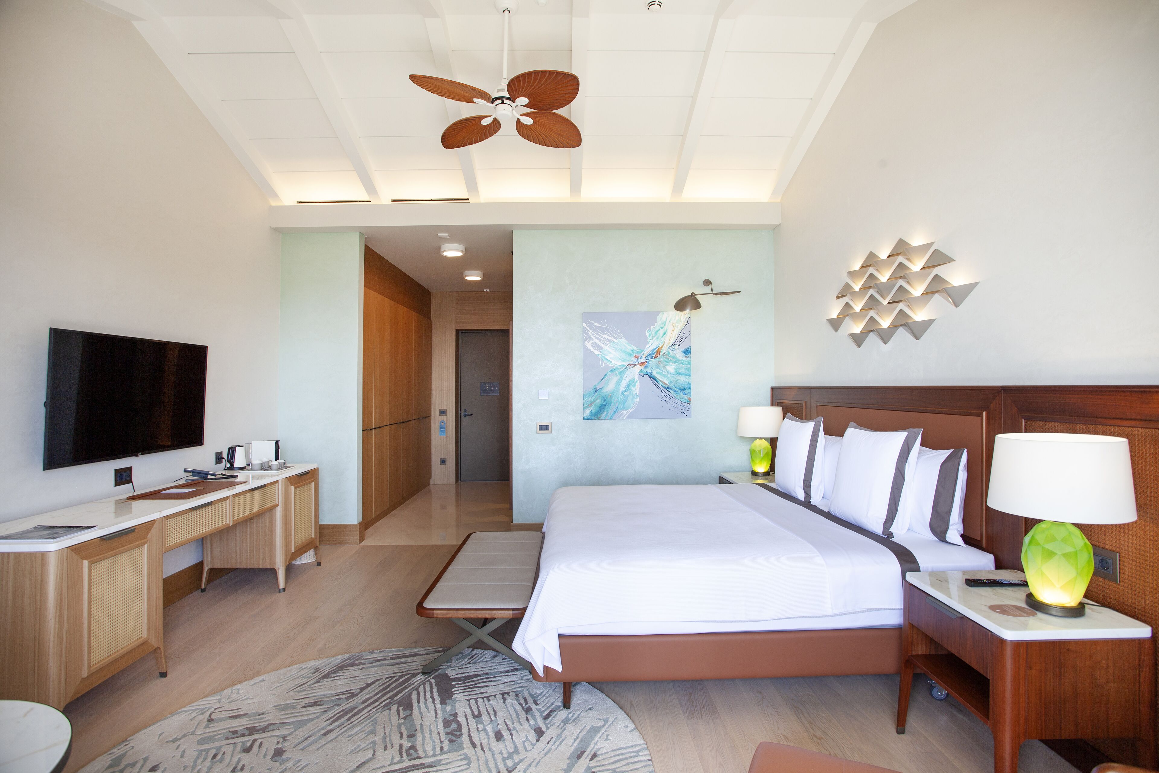 A hotel room with a bed, desk, television, and a ceiling fan.