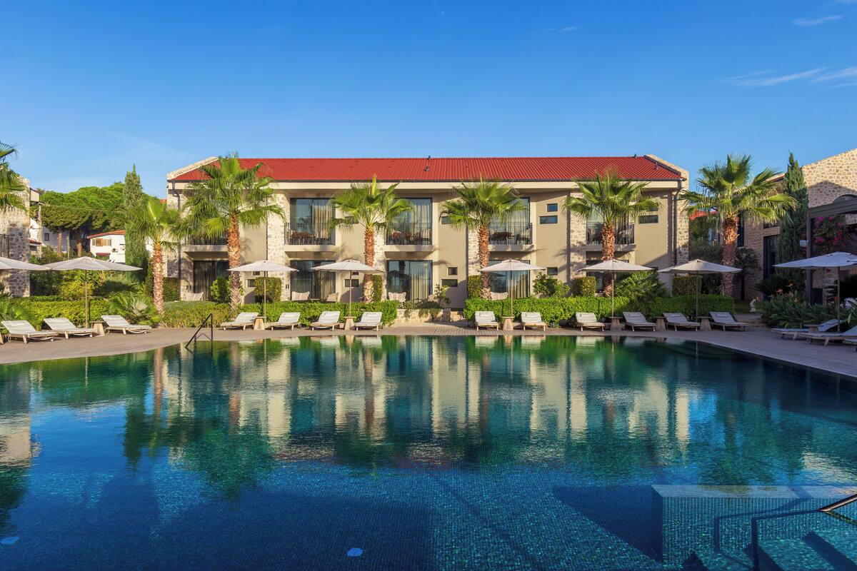 Un hotel con piscina, sillas de descanso y palmeras.