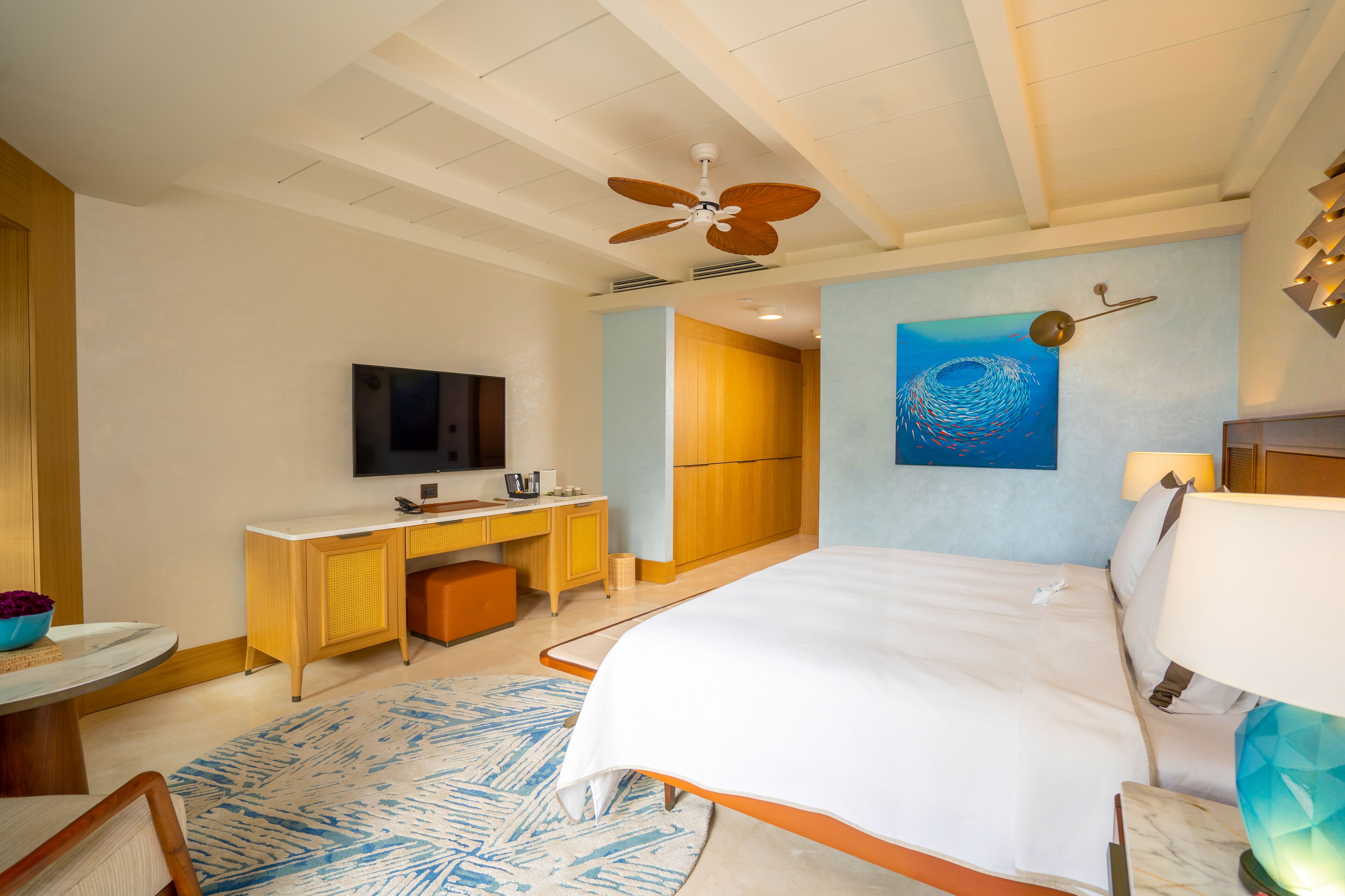 A hotel room with a bed, desk, TV, and artwork on the wall.