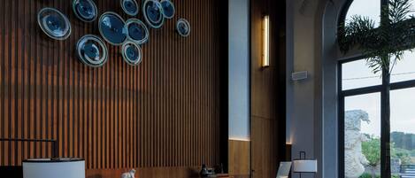 A modern reception area with a wooden panel wall, a large window with a view, and a reception desk with a lamp and a potted plant.