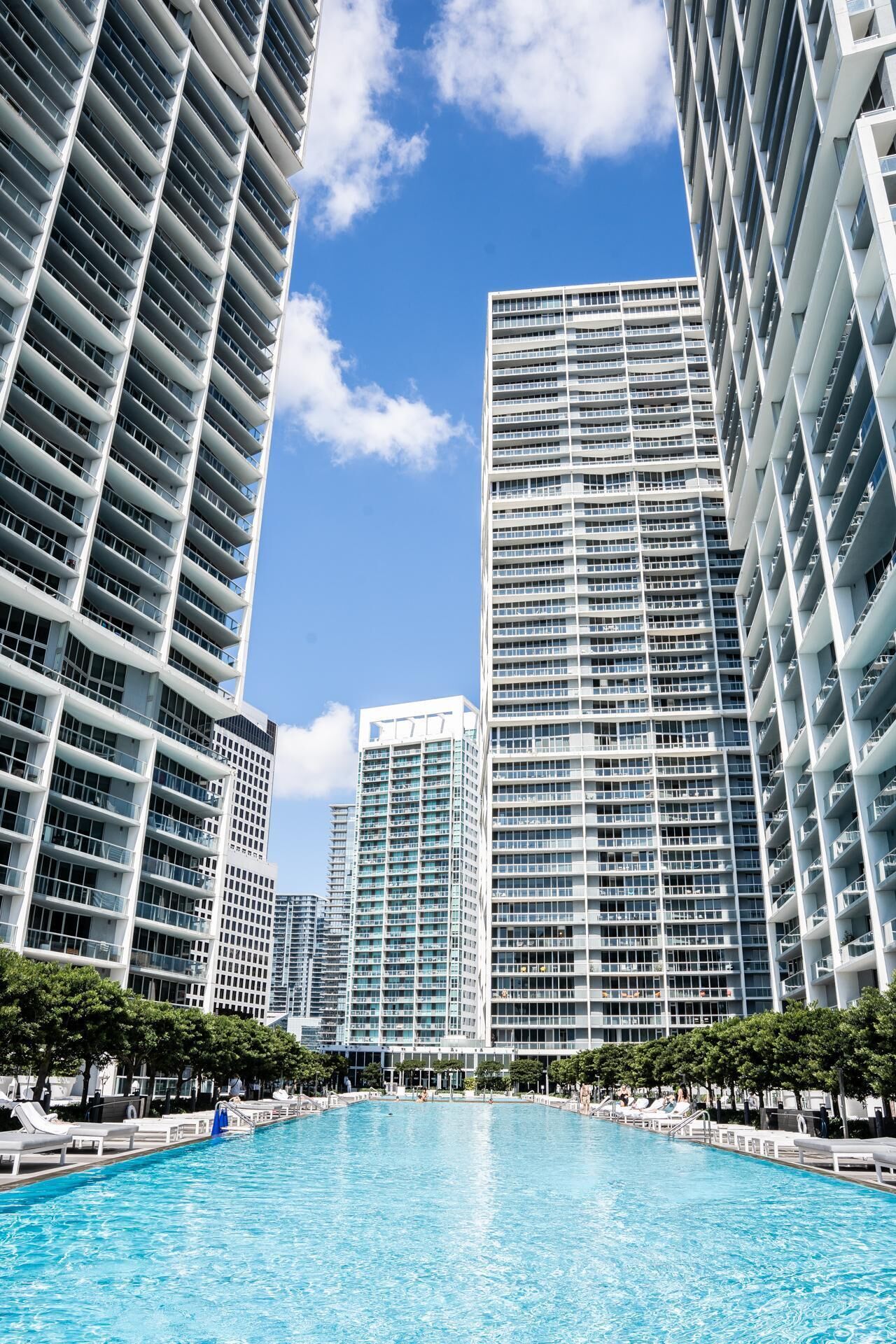 A modern high-rise hotel with a central swimming pool surrounded by lush greenery.