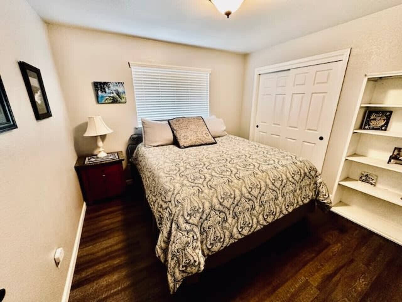Un dormitorio con cama, mesita de noche, lámpara y una puerta.