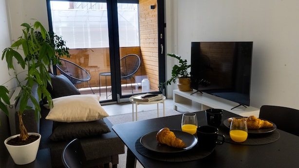 Ett modernt vardagsrum med en soffa, ett soffbord, en tv och en matplats med frukosttillbehör.