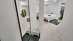 Habitación de hotel moderna con un espejo grande, una cama con manta gris, una mesita con una planta y una alfombra gris.