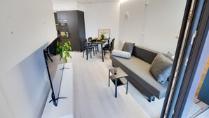 Una sala de estar moderna con un sofá gris, una mesa de comedor con sillas y una cocina al fondo.