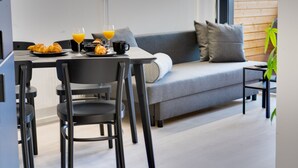 Un comedor moderno con un sofá gris, sillas negras y productos para el desayuno, como cruasanes y jugo de naranja.