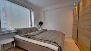 Un dormitorio moderno con una cama, una mesita pequeña, una planta en maceta y un armario de madera.