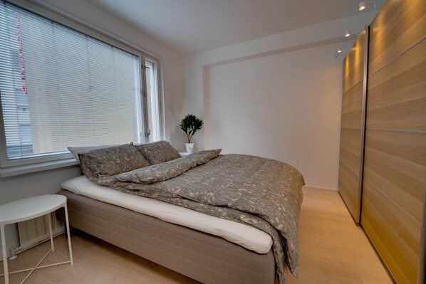 Un dormitorio moderno con una cama, una mesita pequeña, una planta en maceta y un armario de madera.