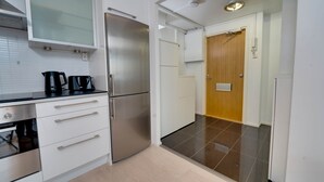 Una cocina moderna con armarios blancos, un refrigerador de acero inoxidable, una cafetera y una puerta de madera que da a otra habitación.