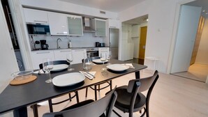 Una cocina moderna con armarios blancos, una encimera negra y una zona de comedor con una mesa dispuesta para cuatro.