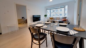 Un comedor moderno con una mesa dispuesta para cuatro, un sofá al fondo y un televisor en la pared.