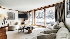 Ein modernes Wohnzimmer mit einer Couch, Sesseln, einem Couchtisch und einem Fernseher.