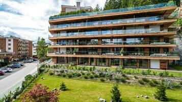 A multi-story building with balconies, a parking lot, and a well-maintained lawn with a statue.