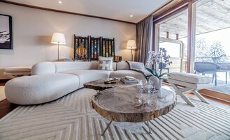 Una sala de estar moderna con un sofá seccional, una mesa de centro de madera y un ventanal con vistas a árboles cubiertos de nieve.