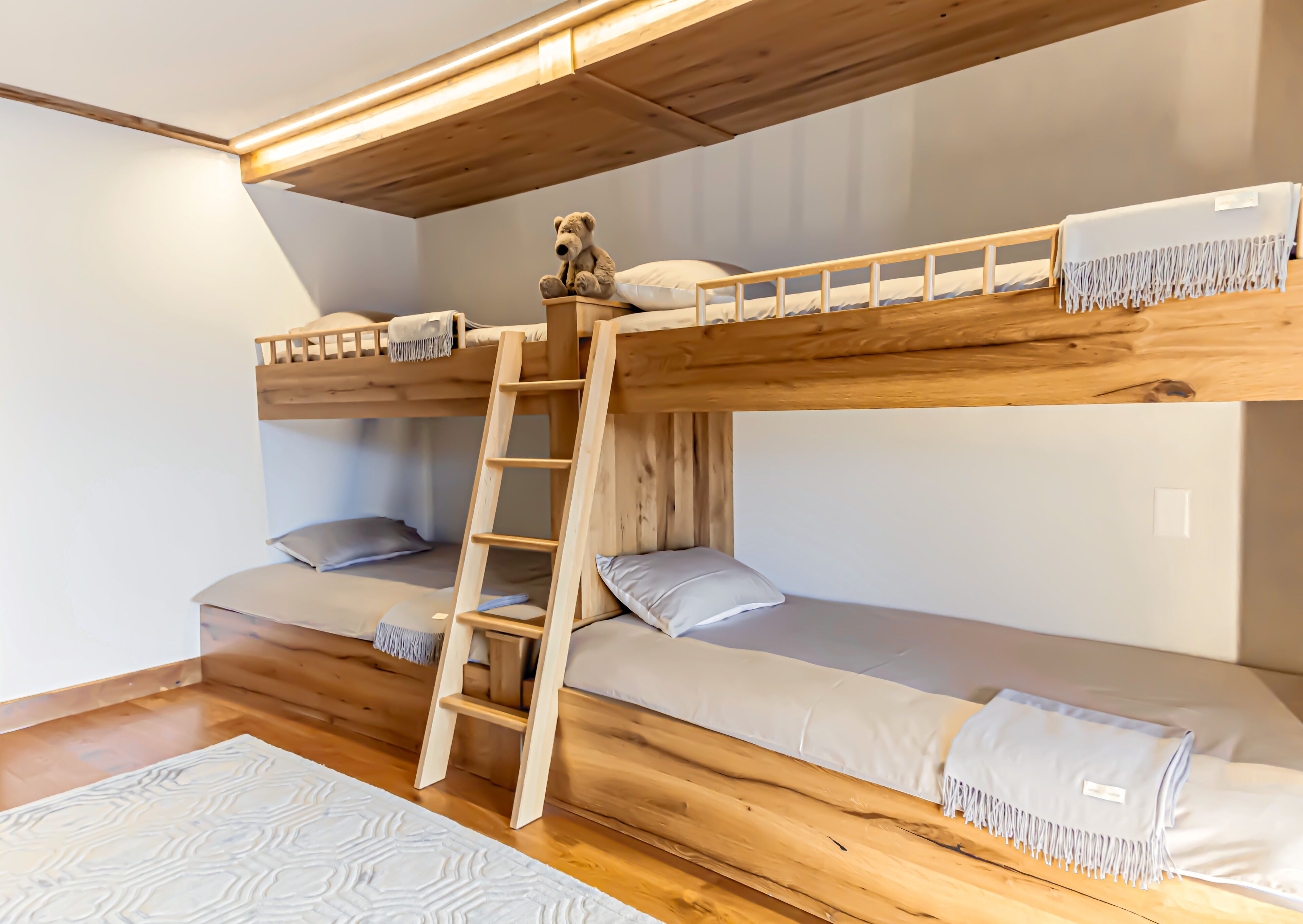 A bunk bed with a wooden ladder, two pillows, and a blanket on each bed.