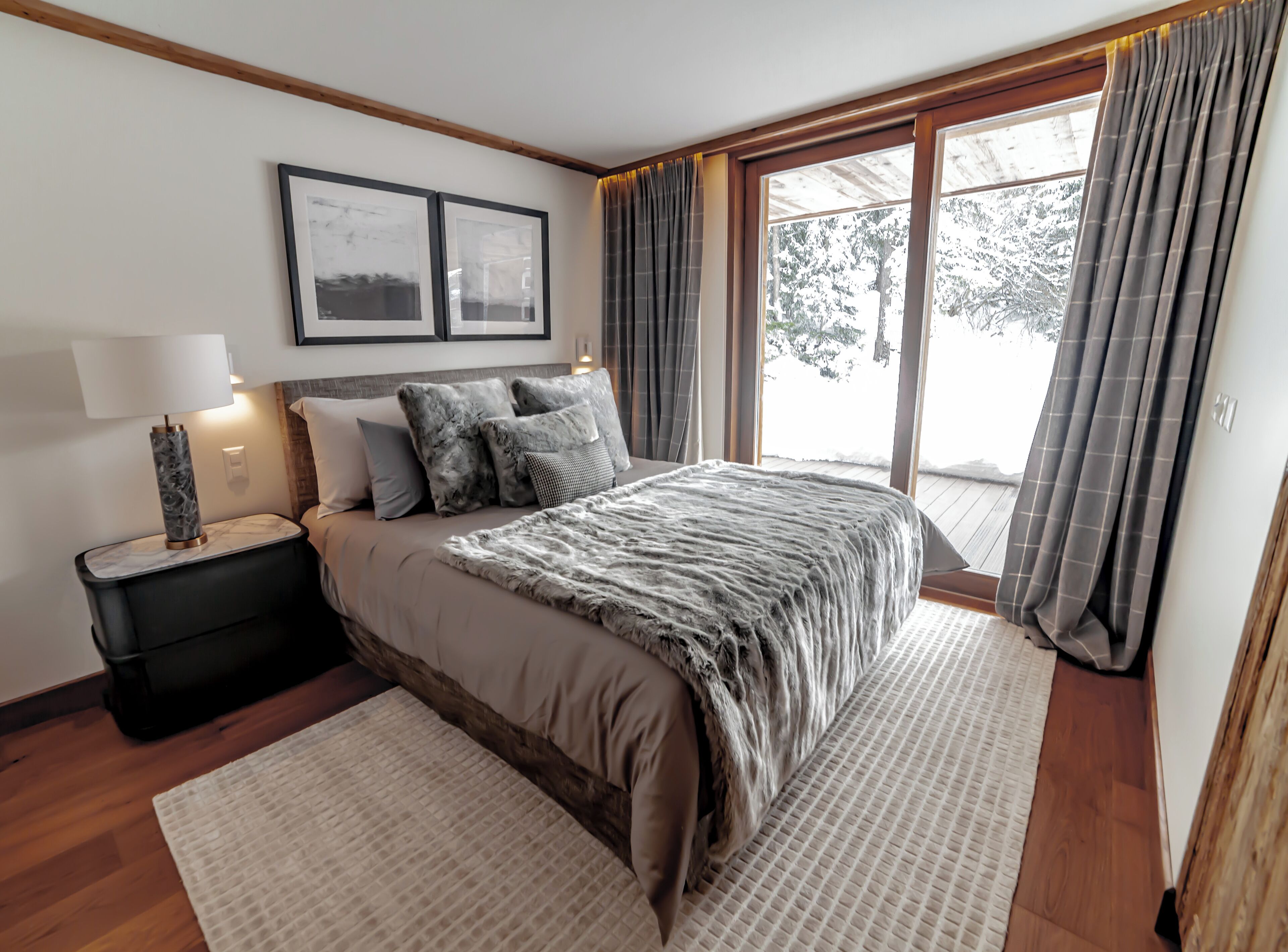 A bedroom with a large bed, a nightstand with a lamp, a window with curtains, and two framed pictures on the wall.