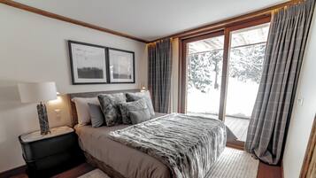 A bedroom with a large bed, a nightstand with a lamp, a window with curtains, and two framed pictures on the wall.