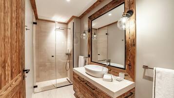 A modern bathroom with a wooden vanity, a large mirror, and a glass shower enclosure.