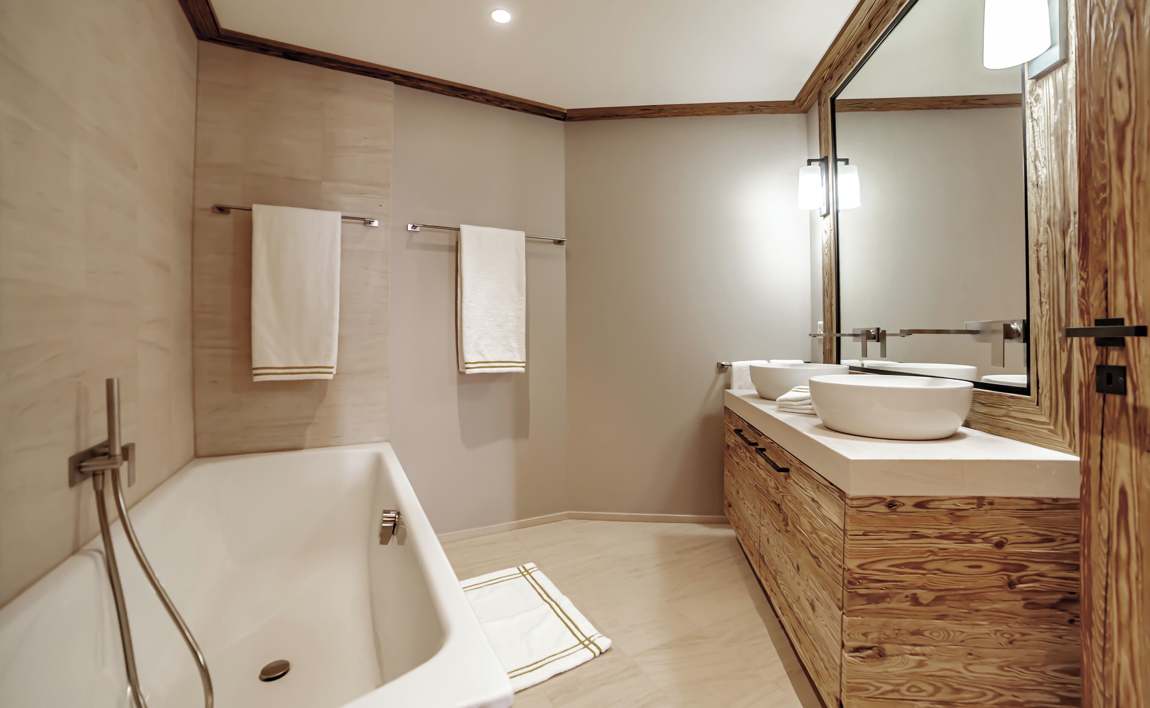 A modern bathroom with a freestanding bathtub, a wooden vanity with a large mirror, and two towels hanging on the wall.
