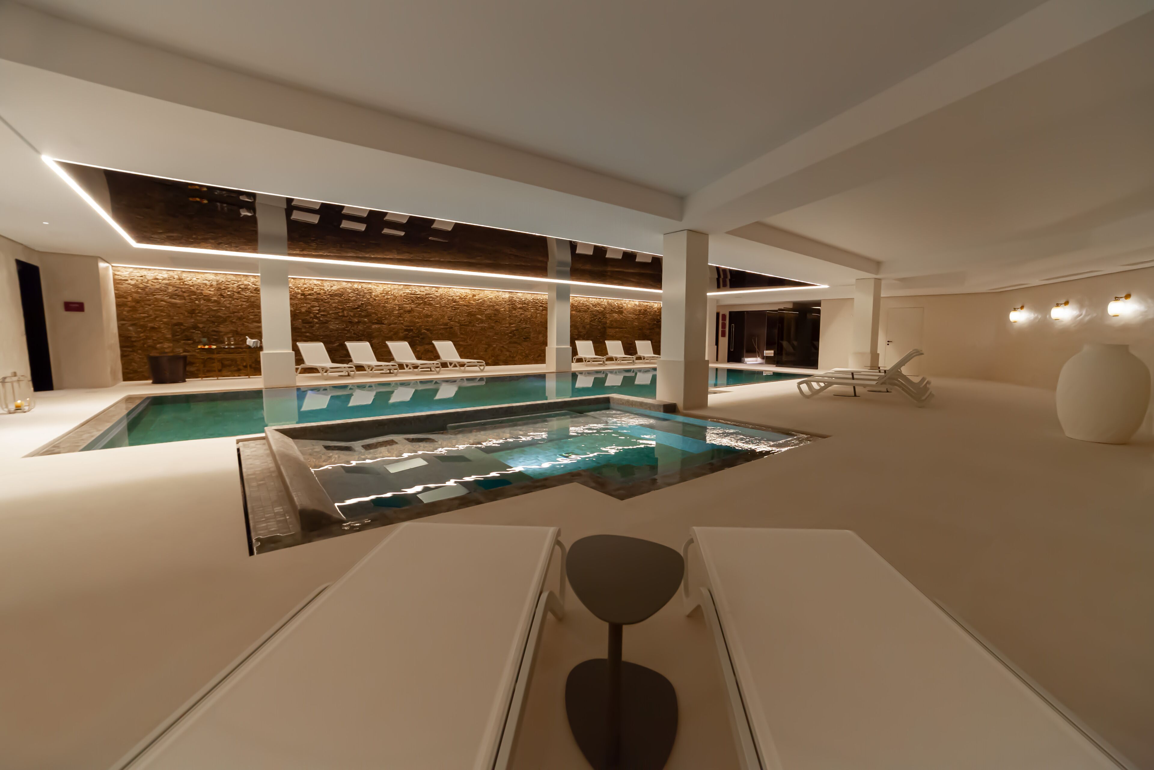 A modern indoor pool area with lounge chairs and a central water feature.