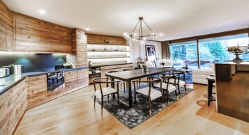 Una cocina moderna con detalles de madera, un comedor con candelabro y un amplio ventanal con vistas al exterior.