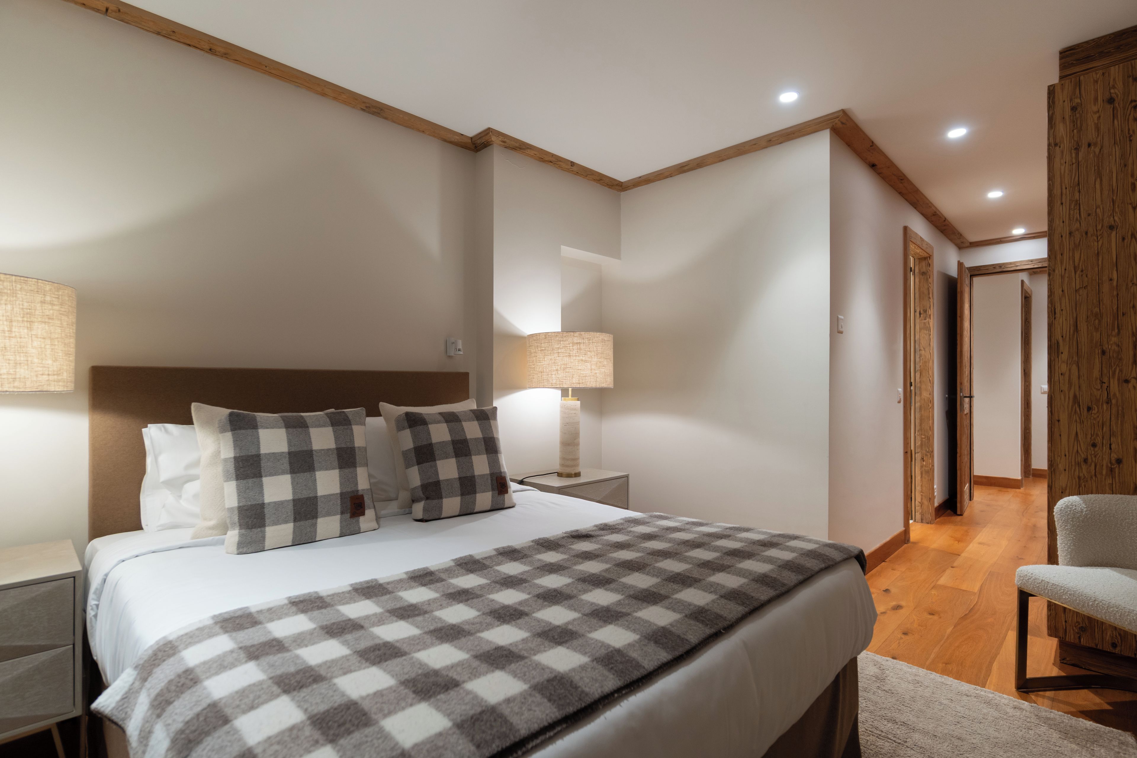 Une chambre à coucher avec un lit, deux lampes de chevet, un plaid à carreaux, une tête de lit en bois et une porte en bois.