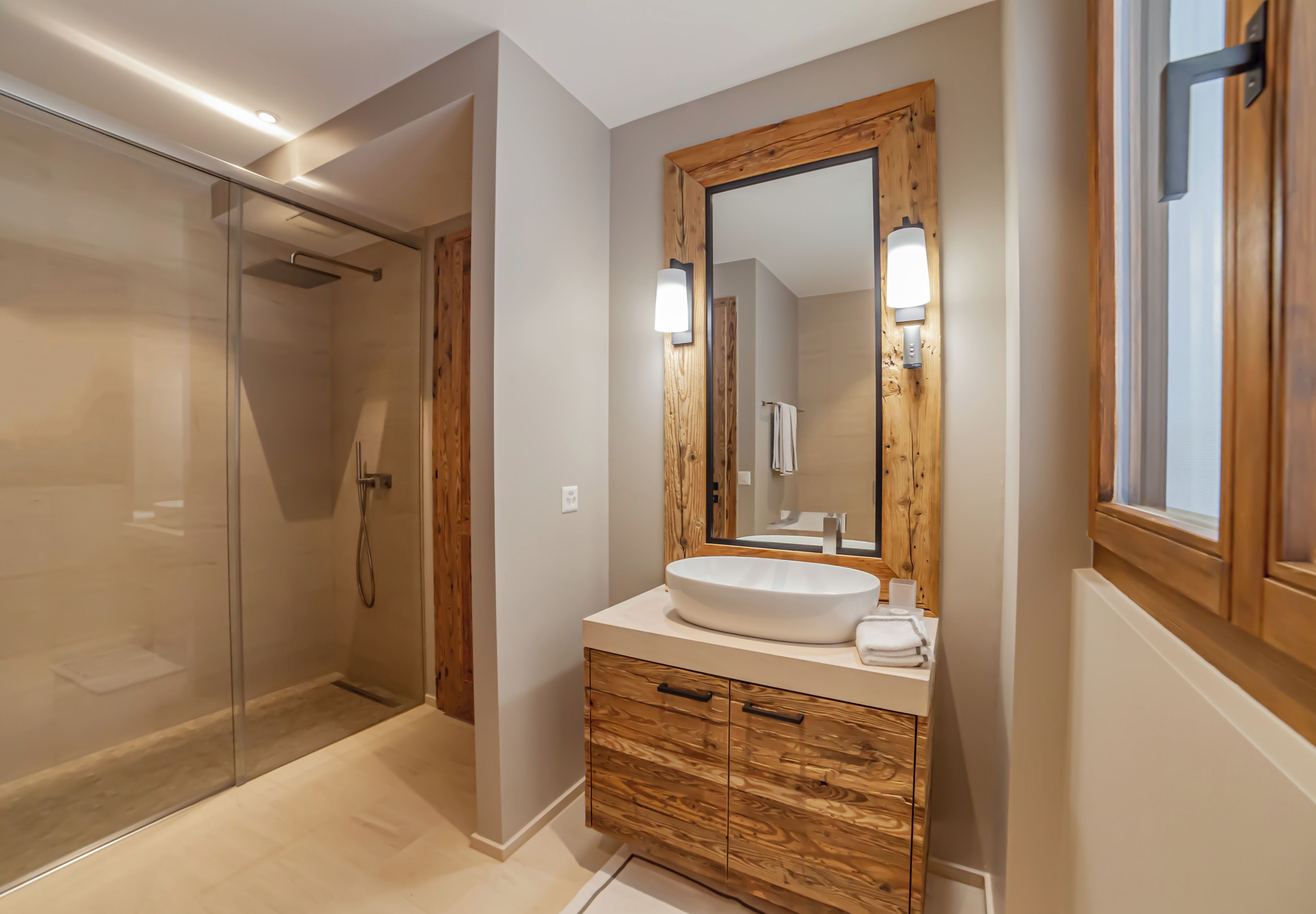 A modern bathroom with a glass shower enclosure, a wooden vanity with a large mirror, and a white sink.