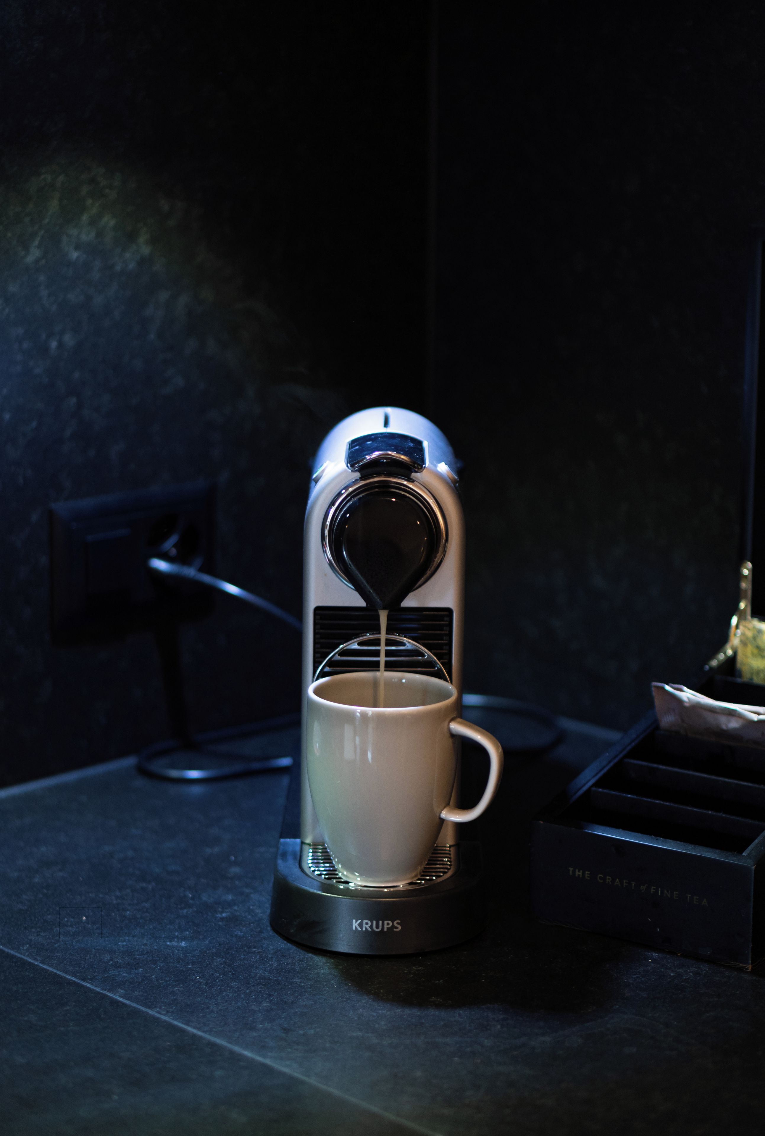 A Krups coffee maker on a dark countertop with a white mug underneath.