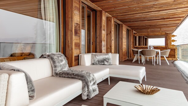 Ein moderner Außenbereich mit weißen Sofas und einem weißen Couchtisch, Holzdielenboden und Blick auf den Ozean.