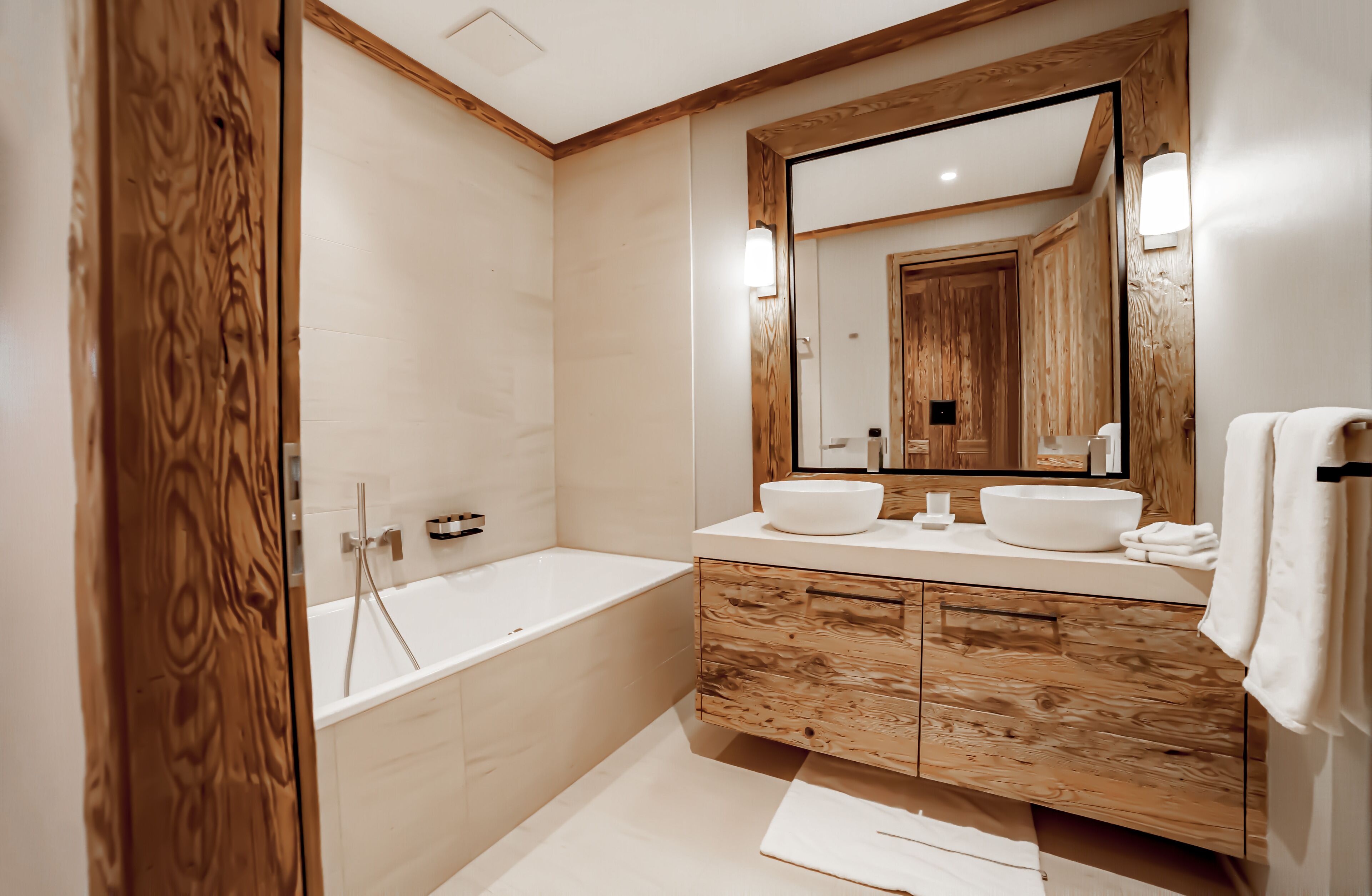 A modern bathroom with a wooden vanity, two sinks, a large mirror, and a bathtub.