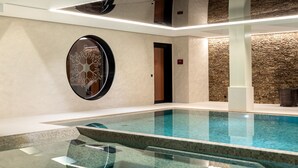 Ein modernes Hallenbad mit klarem Wasser, umgeben von Wänden in neutralen Farbtönen und einer Wand als Akzent in Steinoptik.