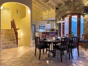 A dining area with a table set for six, a staircase, and a kitchen in the background.