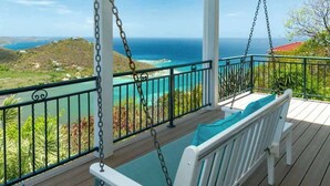 Een houten terras met een schommelstoel, uitzicht op de oceaan en een balustrade.
