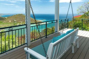 A wooden deck with a swing chair, a view of the ocean, and a railing.