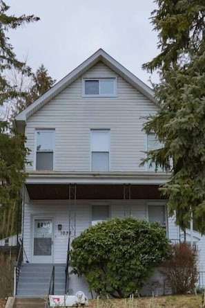 A two-story house with a front porch, a small front yard, and a number '103' on the door.