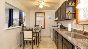 A compact kitchen with a dining area, a ceiling fan, and a window with curtains.