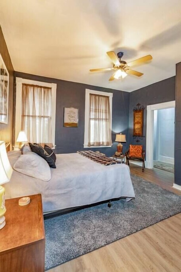 A bedroom with a bed, a ceiling fan, a chair, and a door.