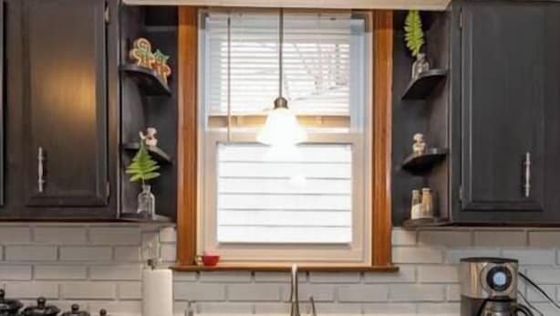 A kitchen with dark wooden cabinets, a granite countertop, a window with blinds, a hanging light fixture, and a coffee maker.