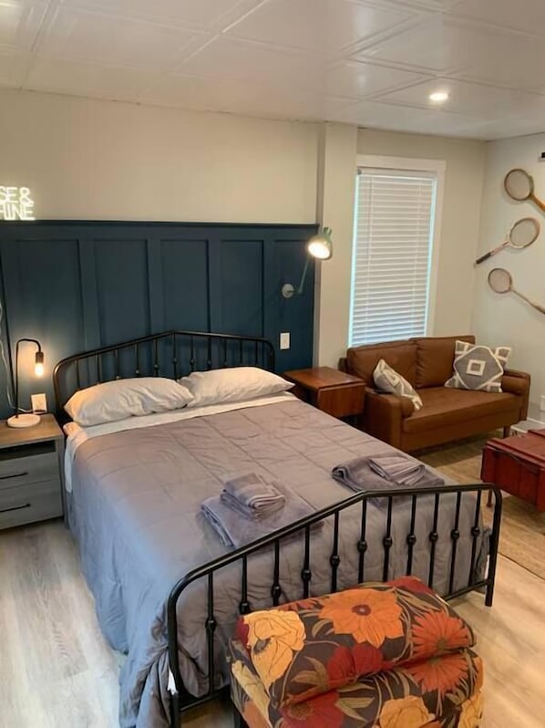 Une chambre à coucher comprenant un lit, une table de chevet, une commode, un canapé et une lampe fixée au mur.