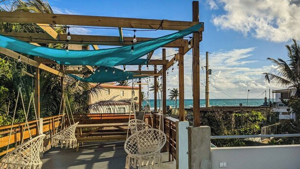 Una terrazza in legno con un'amaca e poltrone in vimini, con vista su una spiaggia e l'oceano.