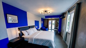 Una camera d'albergo moderna con un letto grande, un comodino e una scrivania laterale con una lampada, oltre a una vista esterna attraverso una finestra.