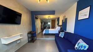 Una camera d'albergo moderna con una parete azzurra, una TV a schermo piatto montata al muro, un divano con cuscini decorati, un letto con lenzuola bianche e un tavolino con vassoio.