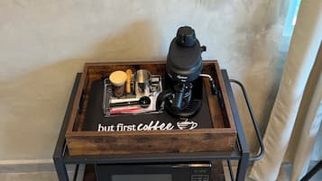 Uma estação de café com cafeteira, xícaras e copos sobre uma bandeja de madeira.