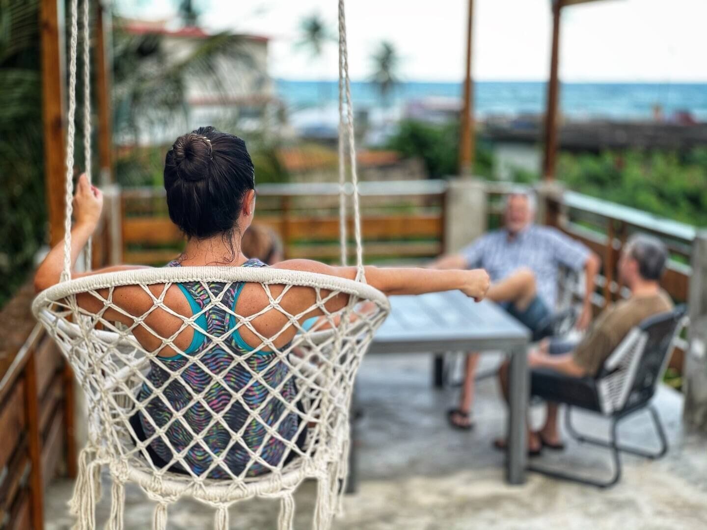 A hammock chair with a person sitting in it, overlooking a patio area with a table and chairs.